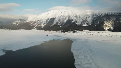 Areal-footage-of-a-half-melted-lake-with-a-snow-covered-mountain-in-the-background-at-sunset