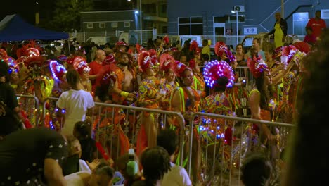 Red-headdress-with-golden-rainbow-costumes-on-woman-holding-drink-up-to-sky-at-night-during-Carnival-Parade