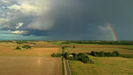 Aerial-view-of-cloudburst-in-countryside-of-Latvia,-agricultural-meadow-covered-in-sunshine