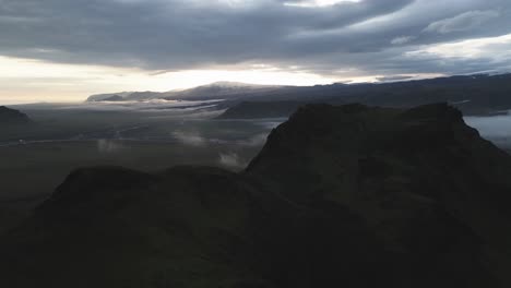 Drohnenkran-über-Dem-Dunklen-Vik-Berg-Enthüllt-Nebliges-Island-Plateau-Im-Lebhaften-Sonnenuntergang