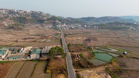 An-aerial-view-capturing-a-vehicle-moving-along-a-straight-roadway-amidst-expansive-paddy-fields