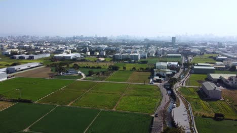 Verdant-farmland-on-city-outskirts-under-clear-skies,-aerial-view