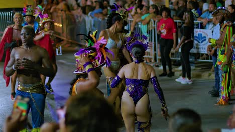 Mujeres-Y-Hombres-Altos-Bailan-Sacudiendo-El-Cuerpo-Bajo-Las-Luces-De-Los-Camiones-Por-La-Noche-Durante-El-Desfile-De-Carnaval