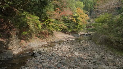 Closeup-at-Kyoto-Japanese-zen-stone-river-valley,-calm-landscape-aerial-drone-flying-low-above-water-in-mountain-temple-vibes,-asian-peaceful-picturesque-view