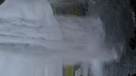 Vertical-Video,-Seljalandsfoss-Waterfall-Iceland,-Under-Falling-Water-on-Dark-Rainy-Day