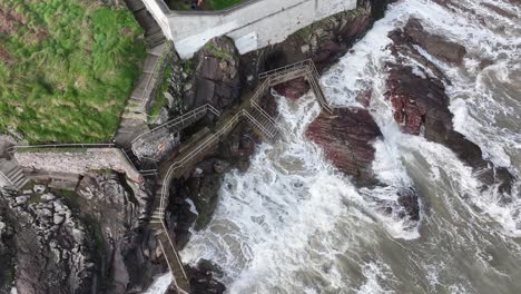 Vídeo-De-Drones-Mirando-Directamente-Hacia-Las-Olas-Rompiendo-Contra-El-Paseo-Y-Las-Rocas-Junto-Al-Faro-De-Youghal-En-Youghal,-East-Cork,-Irlanda