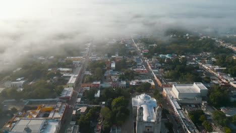 Drone-shot-in-the-foggy-morning-going-by-the-famous-Iglesia-de-San-Servacio-church-revealing-cityscape-of-the-beautiful-city-of-Valladolid,-located-in-the-state-of-Yucatan-in-Mexico-shot-in-4k