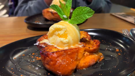 Two-tasty-pain-perdu-French-toasts-with-vanilla-ice-cream-and-fresh-mint-leaves-on-a-plate,-sweet-dessert-at-a-restaurant,-flash-photography-in-the-background,-4K-shot