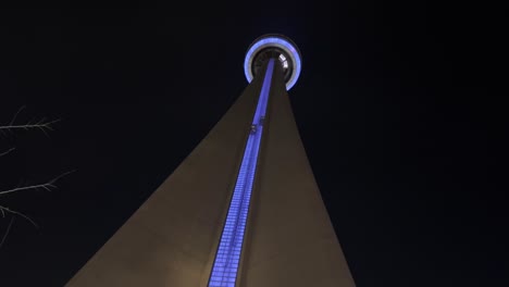 Tilt-up-view-of-CN-Tower-of-Toronto-illuminated-with-elevators-and-rotating-restaurant-on-top-at-night