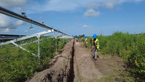 Afrikanische-Arbeiter-Mit-Helm-Und-Sicherheitskleidung-Graben-Einen-Graben-Für-Den-Bau-Eines-Solarkraftwerks-In-Jambur,-Gambia