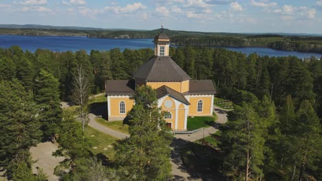 Laukaa-Church,-Finland,-dolly-in-drone-shot-of-the-old-wooden-church-amidst-lakes-and-forest-on-a-beautiful-summer-day
