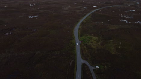 Aerial-drone-tops-down-a-road-Isle-of-Skye-Scotland-through-mountain-valley-car-driving-at-countryside-fields-skyline-with-hills-peak-sunset-light