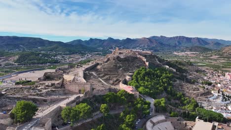 Hochwertige-Aufnahmen-Mit-Einer-Drohne-Eines-Panoramas-Der-Burg-Von-Sagunto-Und-Ihrer-Mauern-Auf-Einem-Hügel-Mit-Einem-Hintergrund-Aus-Bergen-Und-Einem-Blauen-Himmel-Mit-Wolken-In-Valencia,-Spanien