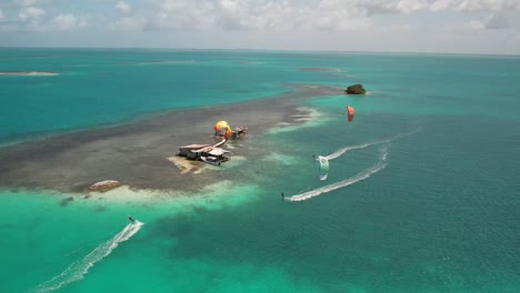 Stilt-house-and-kite-surfers-on-turquoise-sea,-aerial-view