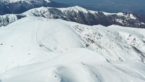 Skifahrer-Säumen-Eine-Weite,-Schneebedeckte-Berglandschaft-Unter-Blauem-Himmel,-Ruhige-Wintersportszene,-Luftaufnahme