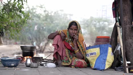 Cinematic-Shot-slow-motion-seen-in-which-Woman-from-a-slum-area-is-seen-sitting-quietly-on-the-pavement-and-preparing-food