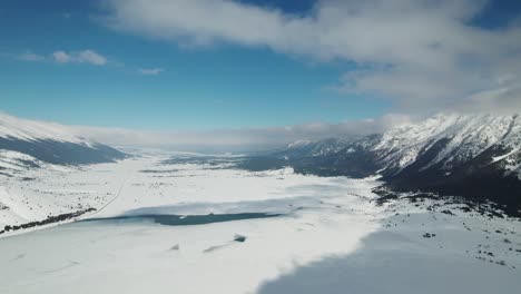 Areal-shoot-of-a-frozen-lake,-surrounded-by-mountains-on-a-beautiful-sunny-day