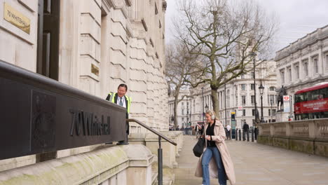 In-slow-motion-a-woman-walks-into-70-Whitehall,-the-entrance-to-the-UK-government-Cabinet-Office,-as-a-security-guard-stands-outside