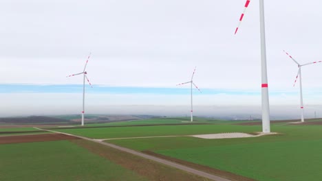 Girando-Turbinas-Eólicas-Gigantes-Sobre-La-Naturaleza-Verde-Al-Amanecer.