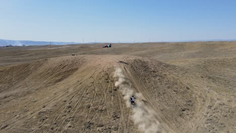 An-action-packed,-slow-motion-drone-shot-of-two-motocross-riders-hitting-a-big-hill-jump,-in-the-desert-like-terrain-of-Grand-Valley-OHV-area,-located-in-Grand-Junction,-Colorado