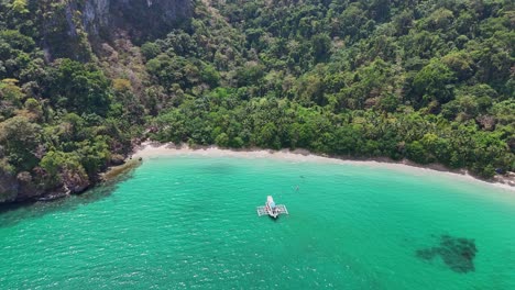 Drone-footage-of-a-filipino-boat-in-a-turquoise-lagoon-near-a-steep-cliff-at-Palawan-in-the-Philippines