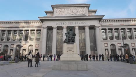 Stabilisierte-Aufnahme-Eines-Spaziergangs-Zum-Eingang-Und-Zur-Skulptur-Des-Museo-Del-Prado-Velazquez-An-Einem-Sonnigen-Wintertag-Mit-Menschen,-Die-Schlange-Stehen