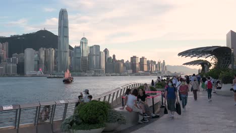 People-spend-their-afternoon-at-the-Victoria-waterfront-as-the-iconic-wooden-red-sail-junk-boat-known-as-Aqua-Luna-sails-across-the-harbor-and-the-Hong-Kong-skyline-as-the-sunset-starts-to-settle-in
