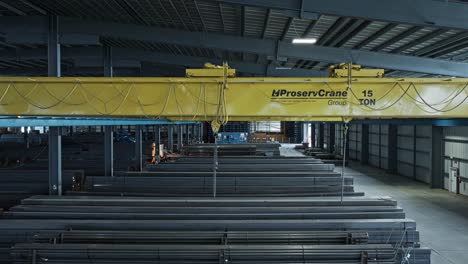 Overhead-bridge-crane-operates-chains-preparing-to-lift-steel-beams-in-warehouse