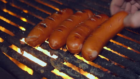 Bratwurst-sausages-cook-on-open-fire-grill-outdoors,-closeup-hand-turn