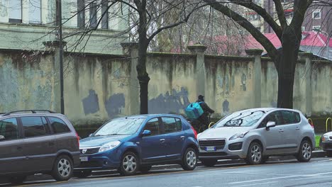 Cyclist-heading-onwards,-automobiles-parked-on-Milan-city-roadside