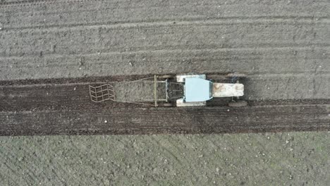 Aerial-top-down-view-of-old-soviet-tractor-with-harrow-on-brown-soil-farmland