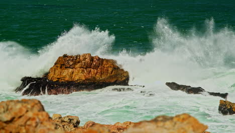 Aquamarinblaue-Meereswellen-Brechen-über-Felsen-Und-Erzeugen-Schäumende-Gischt,-Teleobjektiv