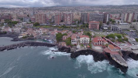 Toma-Aérea-De-La-Costa-De-Catania,-Sicilia,-Italia-Con-Olas-Del-Mar-Rompiendo-En-El-Acantilado-Volcánico