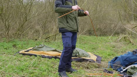 Assembling-the-tent-poles-in-preparation-for-pitching-a-tent,-an-outdoorsman-is-at-a-campground-in-the-middle-of-Thetford-forest-in-Brandon,-United-Kingdom