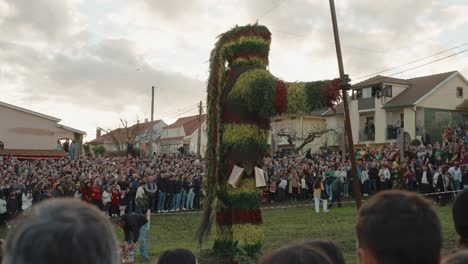 Large-crowd-gathered-around-Giant-Careto-Figure-at-folk-Carnival,-Podence-Portugal