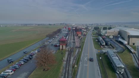 An-Aerial-View-of-a-Train-Station,-with-a-Steam-Passenger-Train-Approaching-in-the-Distance,-on-a-Partially-Sunny-Day