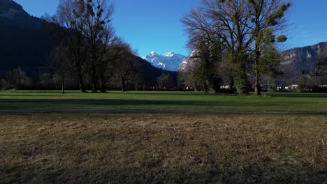 Drohnenansicht-Aus-Niedriger-Perspektive-Auf-Ein-Grünes-Feld-Mit-Den-Schweizer-Alpen-Im-Hintergrund-Am-Walensee,-Schweiz
