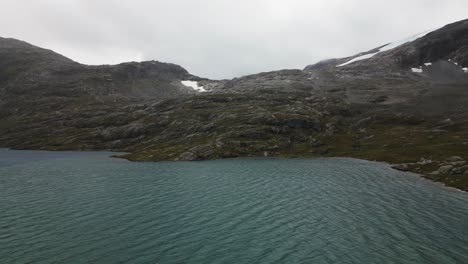 Gran-Lago-Azul-Con-Un-Glaciar-En-Medio-De-Una-Llanura-En-Una-Cadena-Montañosa-Rocosa,-Noruega,-Europa,-Drone