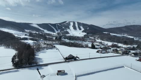 Push-in-drone-shot-flying-above-snow-covered-fields,-with-ski-area-and-mountain-town-in-distance