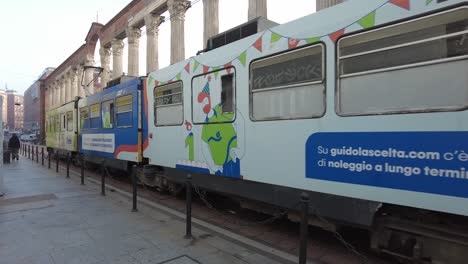 A-tram-streetcar-drives-in-front-of-ancient-roman-pillars-on-the-streets-of-Milan,-Italy