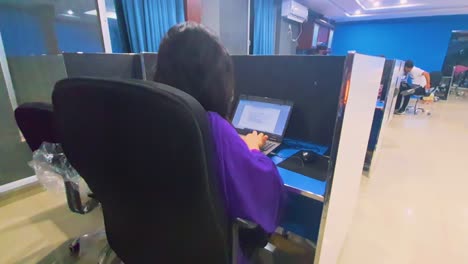 Bei-Einem-Kurzen-Blick-In-Das-Callcenter-Sehen-Wir-Eine-Mitarbeiterin-In-Lilafarbenem-Outfit,-Die-Fleißig-Auf-Ihrem-Laptop-Tippt-Und-Völlig-In-Ihre-Aufgaben-Vertieft-Ist