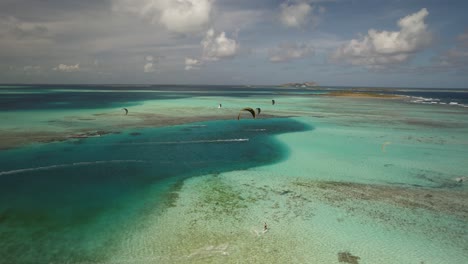 Kite-surfers-glide-over-crystal-clear-waters-near-cayo-vapor,-aerial-shot,-sunny-day
