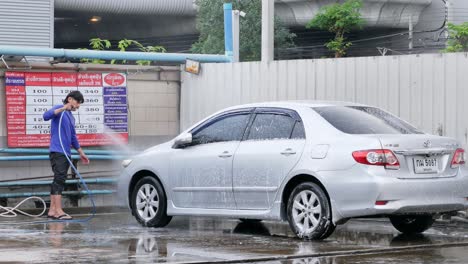 Lavacoches-Lavando-Y-Rociando-Agua-Jabonosa-En-Un-Sedán-En-Una-Tienda-De-Lavado-De-Autos-Ubicada-En-Bangkok,-Tailandia