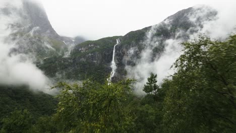 waterfall-running-down-a-big-rock,-green-forrest-with-clouds,-norway,-nature,-drone