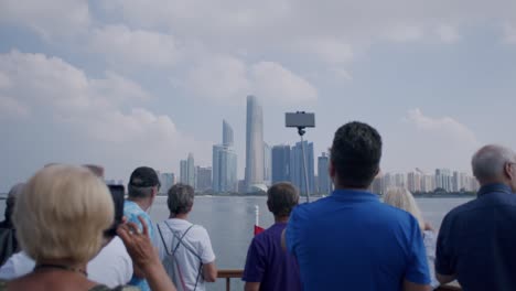 Tourist-on-Cruise-Boat-Taking-Photos-and-Videos-of-Abu-Dhabi-Cityscape-Skyline