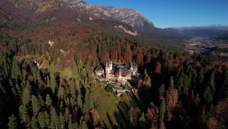 Peles-castle-with-autumnal-forest-backdrop,-in-the-warm-light-of-the-sun,-aerial-view