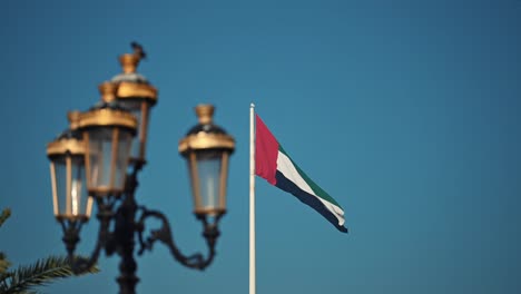 The-UAE-flag-waving-on-the-flagpole,-framed-by-traditional-lamp-post,-at-Sharjah-Flag-Island-in-the-United-Arab-Emirates