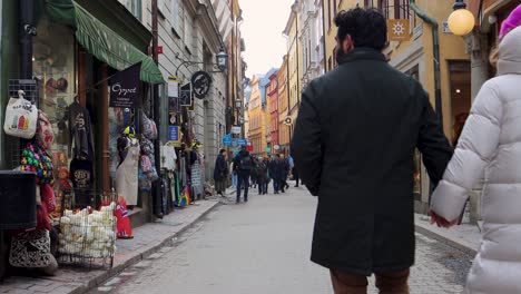 Families-walk-down-cobblestone-street-and-stop-to-look-at-tourist-storefront,-Stockholm