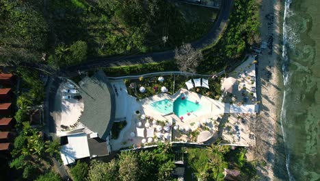 Top-down-aerial-view-of-a-swimming-pool-with-umbrellas-and-lounge-in-the-Cactus-Beach-Club-in-Nusa-Penida,-Bali,-Indonesia