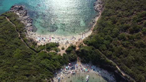 Slide-Aerial-over-Crowed-Porto-Timone-Beach,-Corfu,-Greece